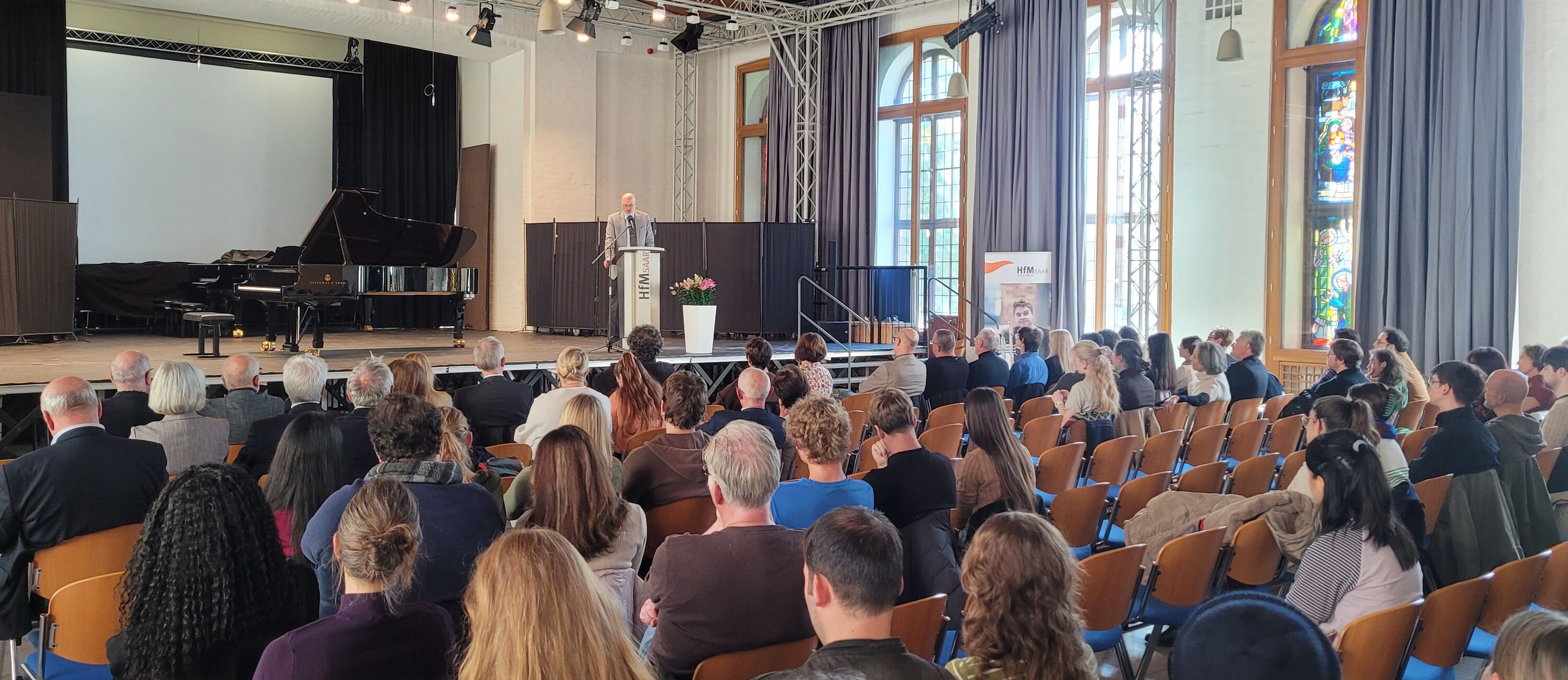 Mann am Rednerpult, davor das Publikum